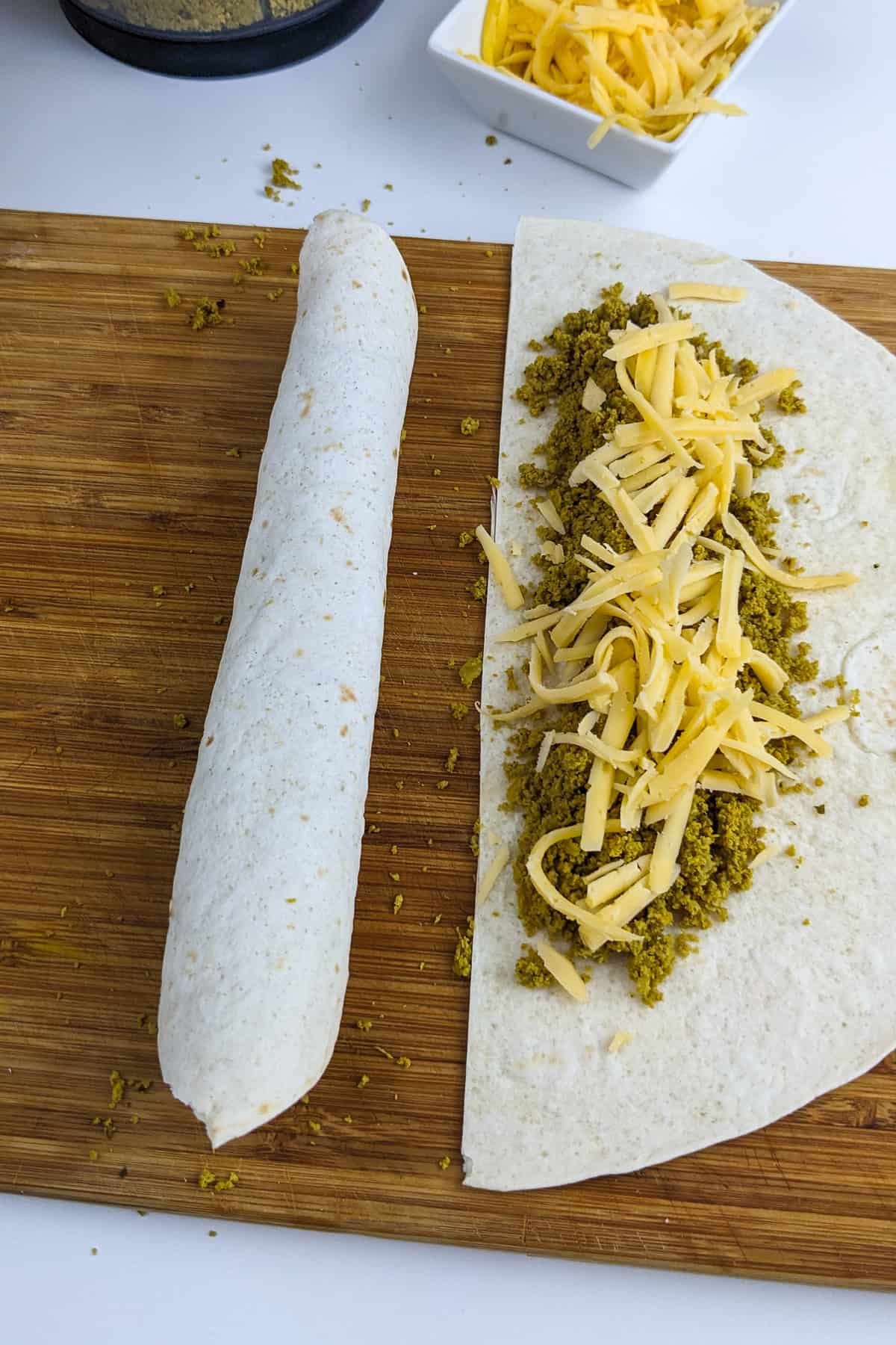Rolled tortilla to form a beef crispitos on a wooden cutting board.
