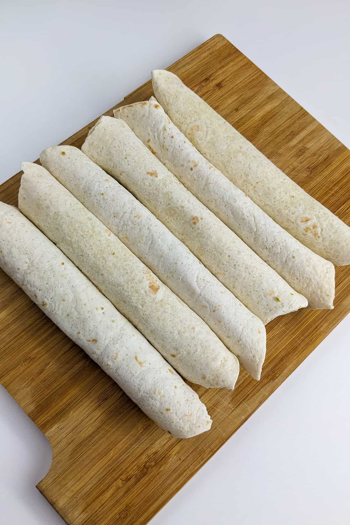 6 rounded crispitos with beef and cheese on a wooden cutting board.