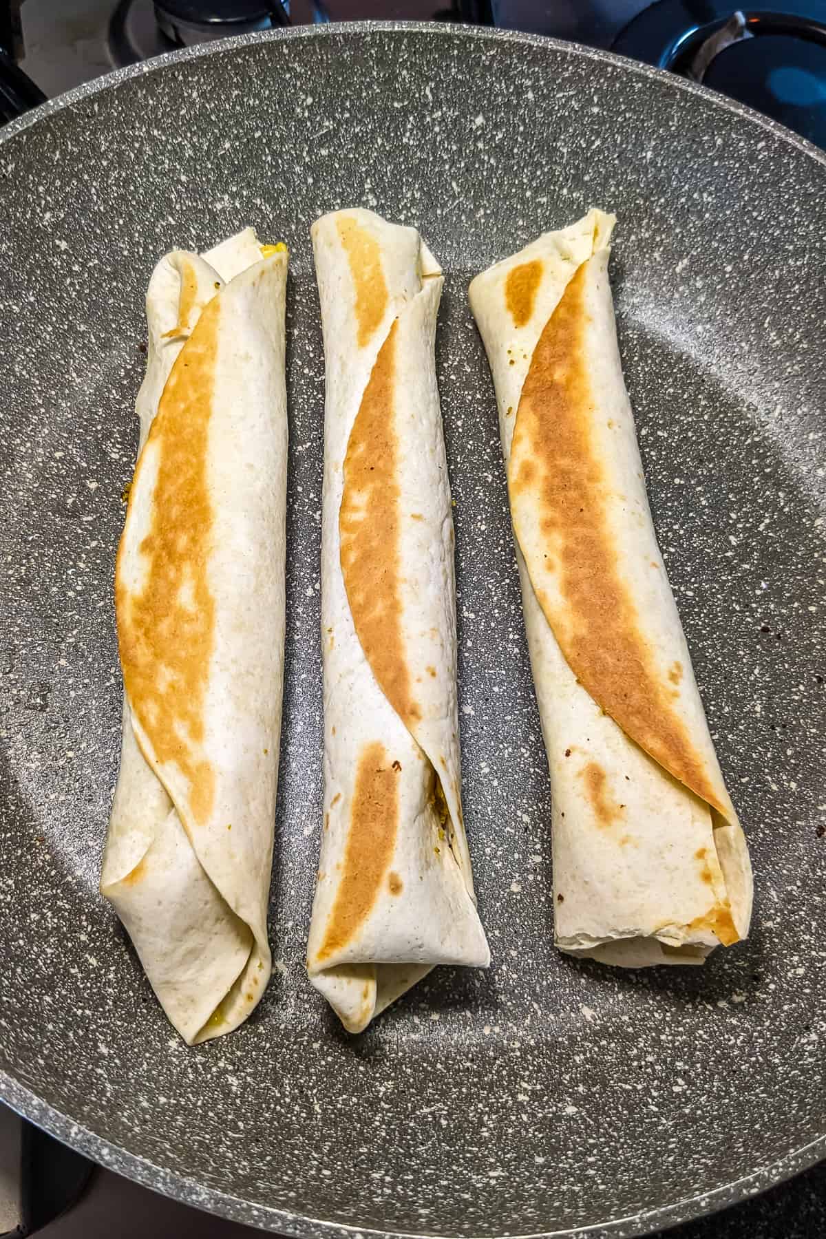 3 rolled fried crispitos on a frying pan.