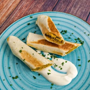 Close look of crispitos halves served with sour cream and chopped parsley.