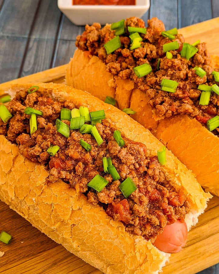Close look of hot dog with ground beef and green onions.