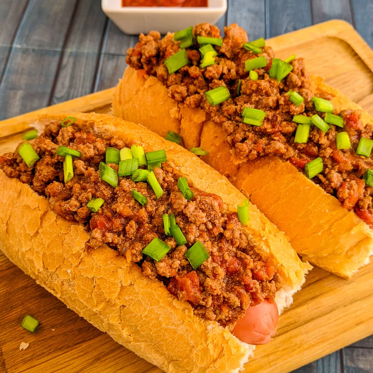 Close look of hot dog with ground beef and green onions.