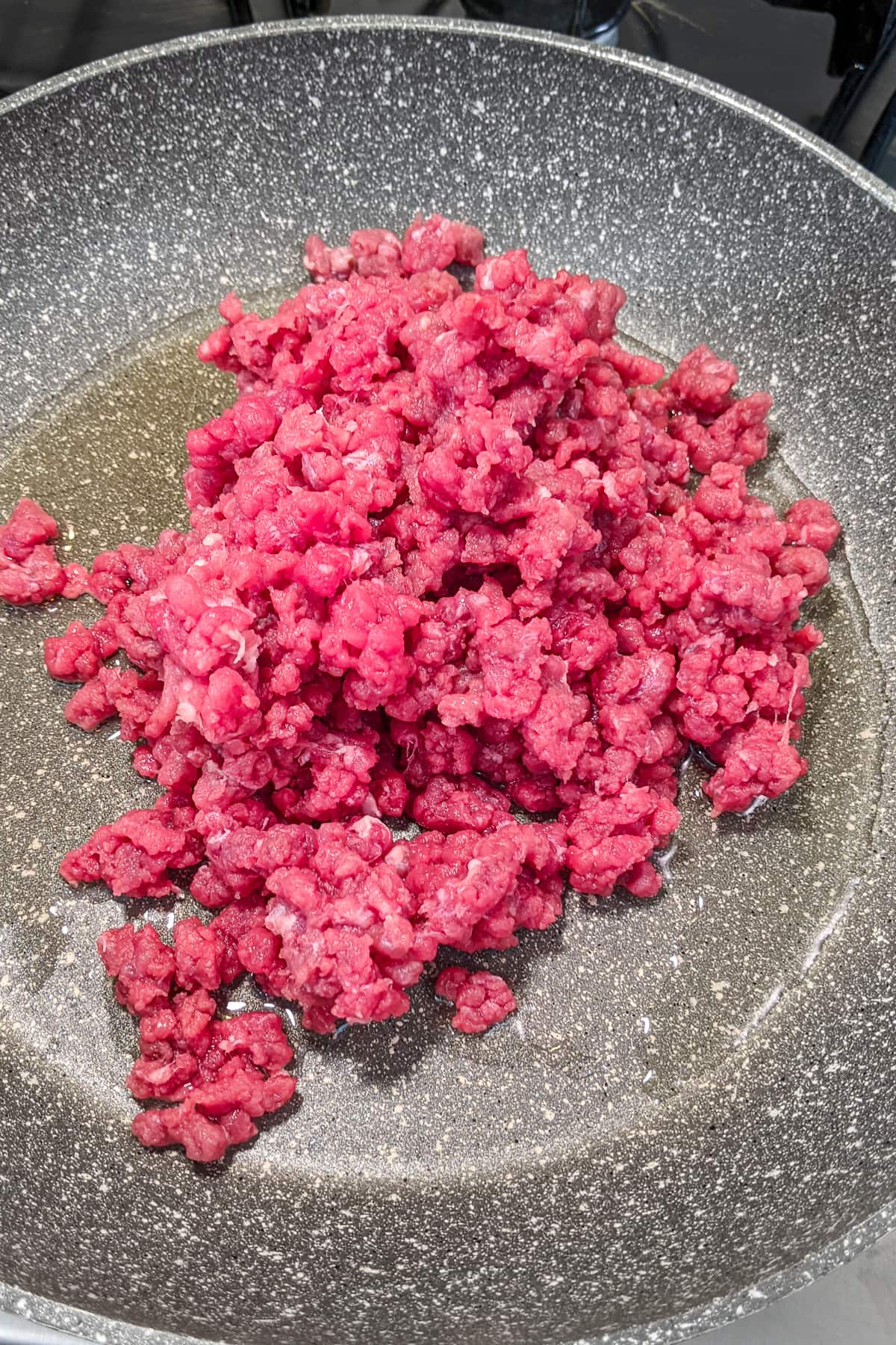 Ground beef with oil in a frying pan.