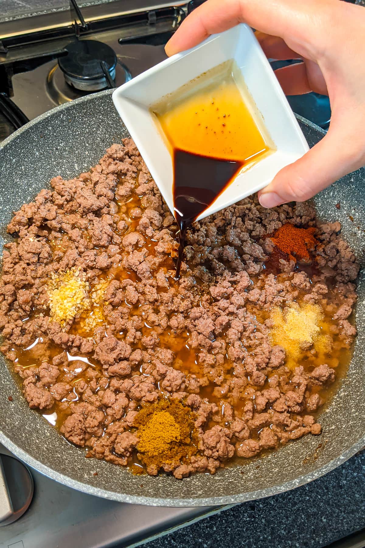 Pouring Worcestershire over frying ground beef.