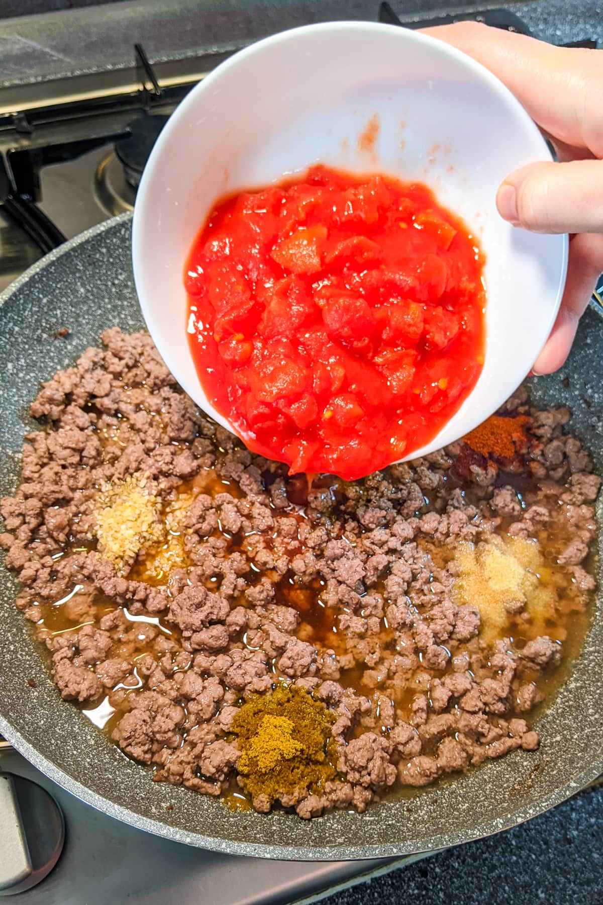 Pouring tomato sauce over fried ground beef.
