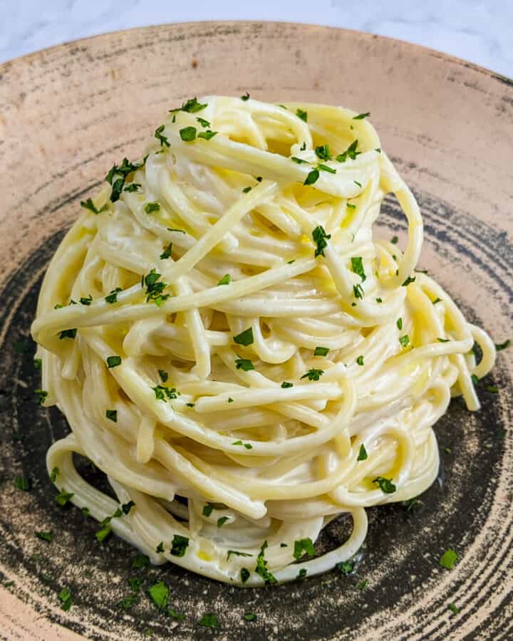 Close look of a plate with pasta with cream cheese and chopped parsley.