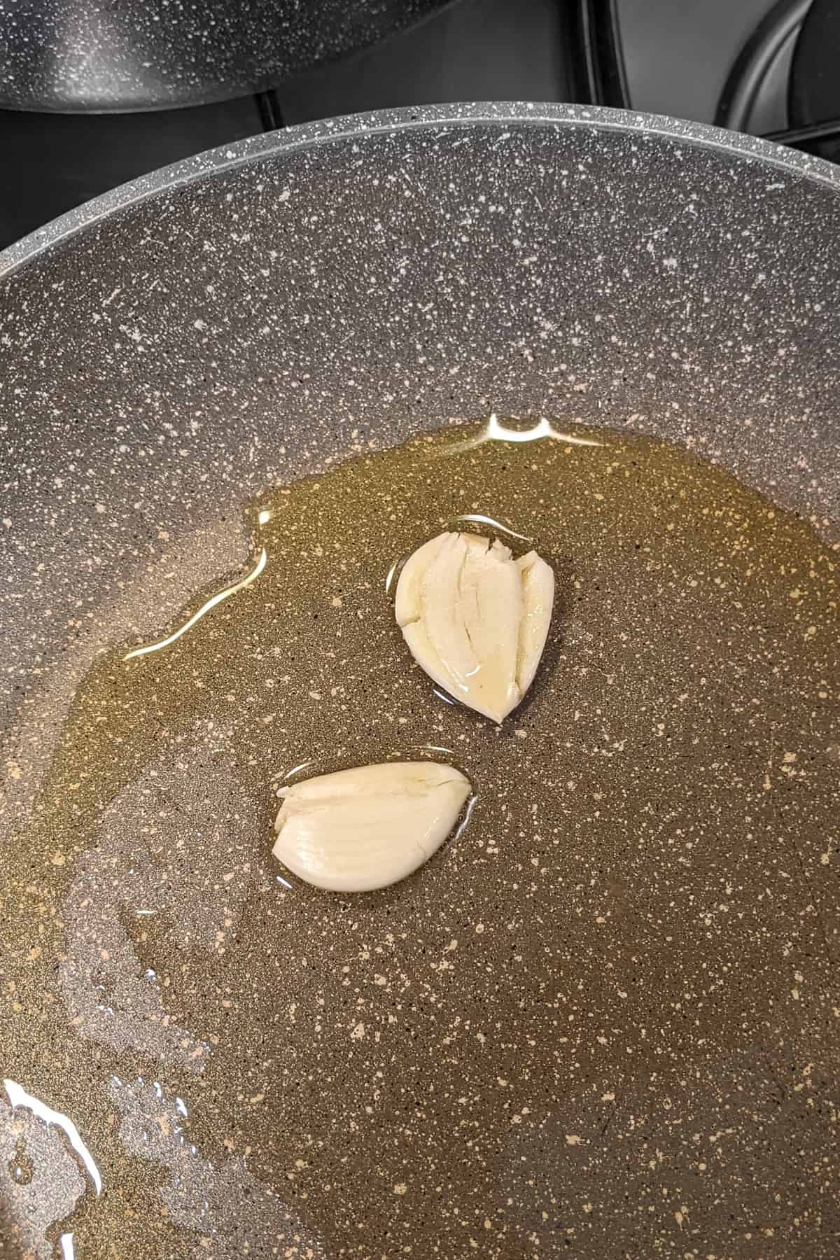 Close look of two crushed garlic cloves frying in olive oil.