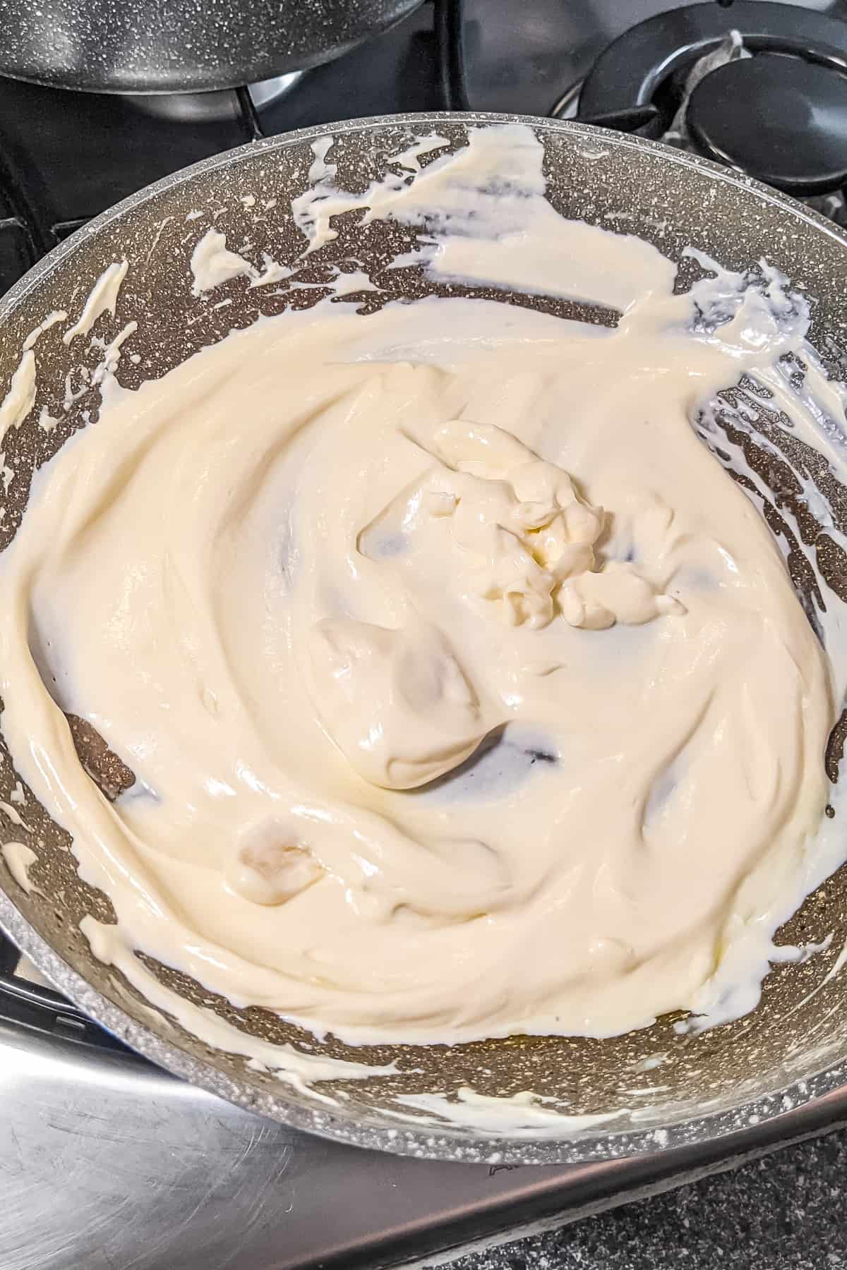 Melted cream cheese in a frying pan on a stove.