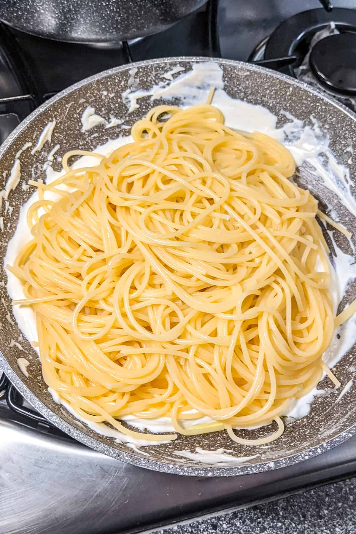 Cooked pasta over melted cream cheese in a frying pan.