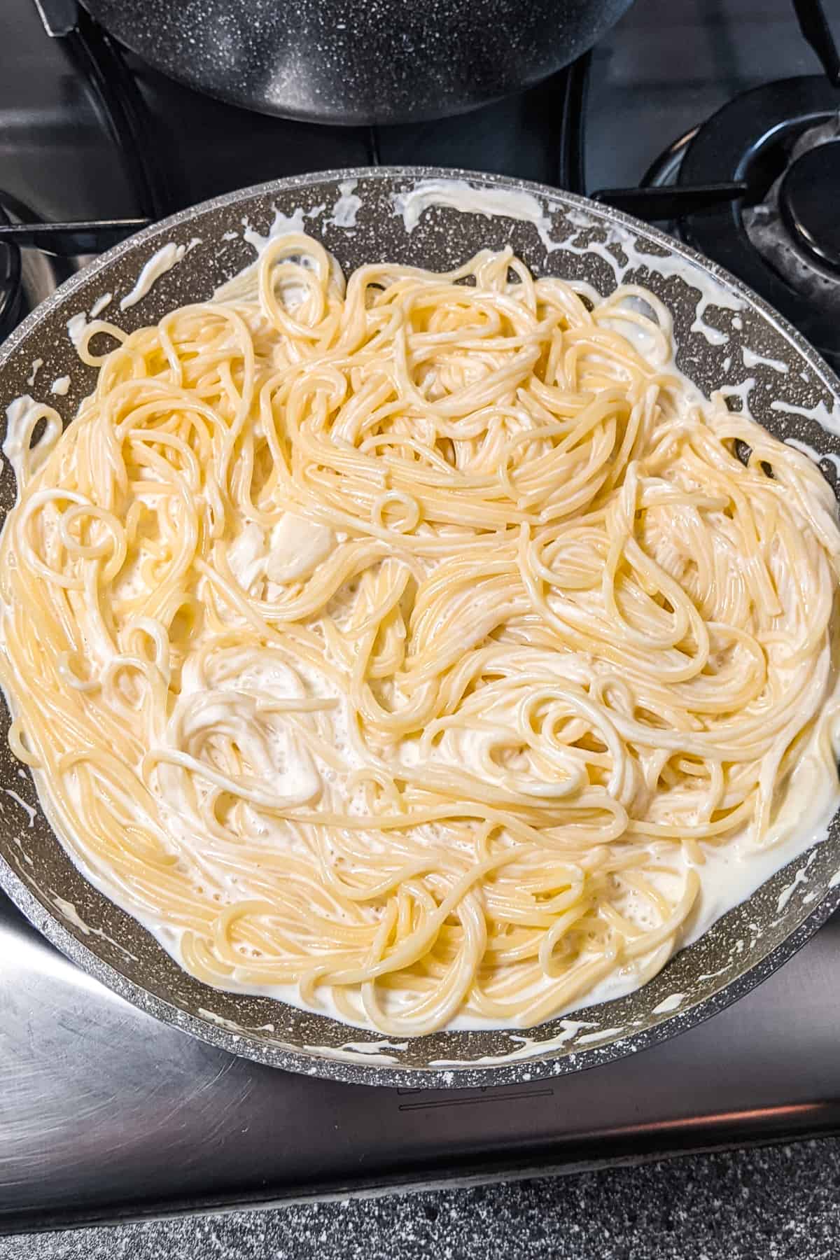 Cooked pasta mixed with melted cream cheese in a frying pan.