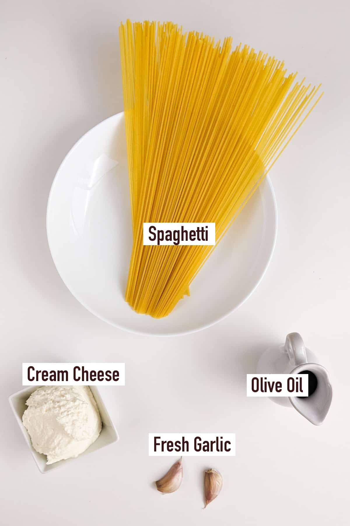 Top view of a white plate with spaghetti, cream cheese, fresh garlic and olive oil.