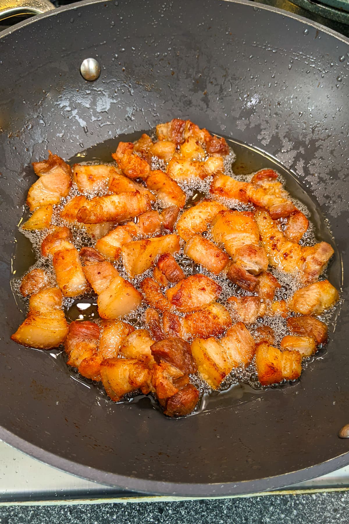 Frying pork belly in a deep wok on the stove.