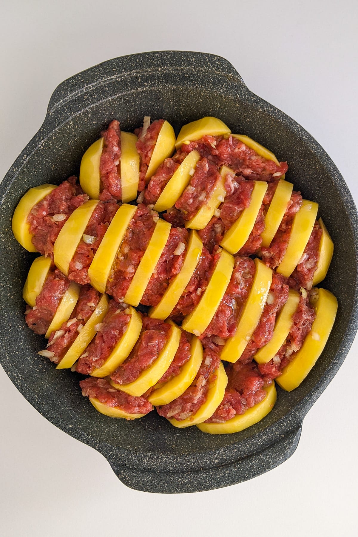 Sliced potatoes with ground beef burgers in a casserole.