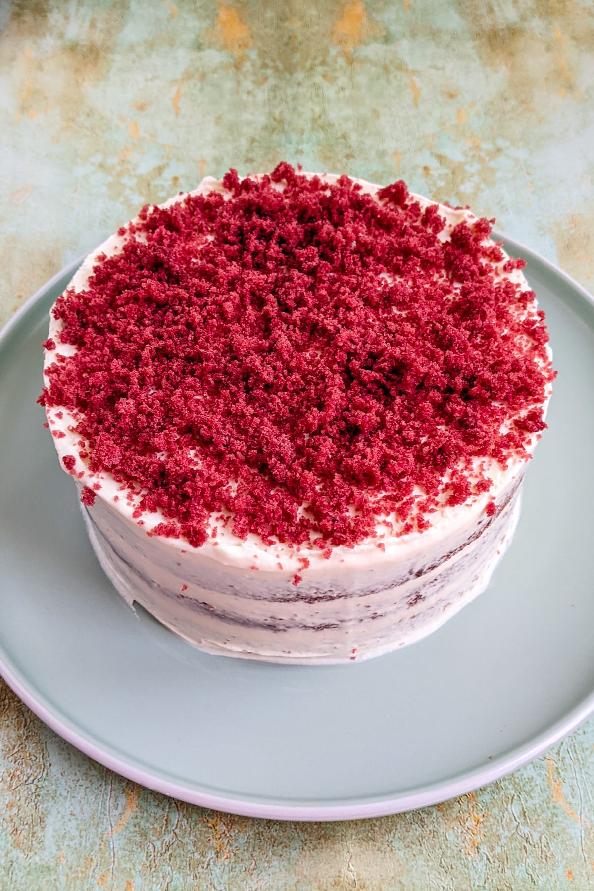 Top red velvet cake on a light blue plate on a marble table.