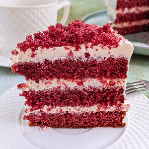 Close look of a slice of red velvet cake sitting on a white plate.