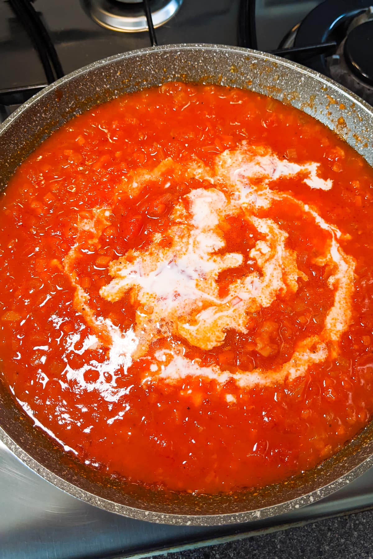 Adding cream over tomato sauce.