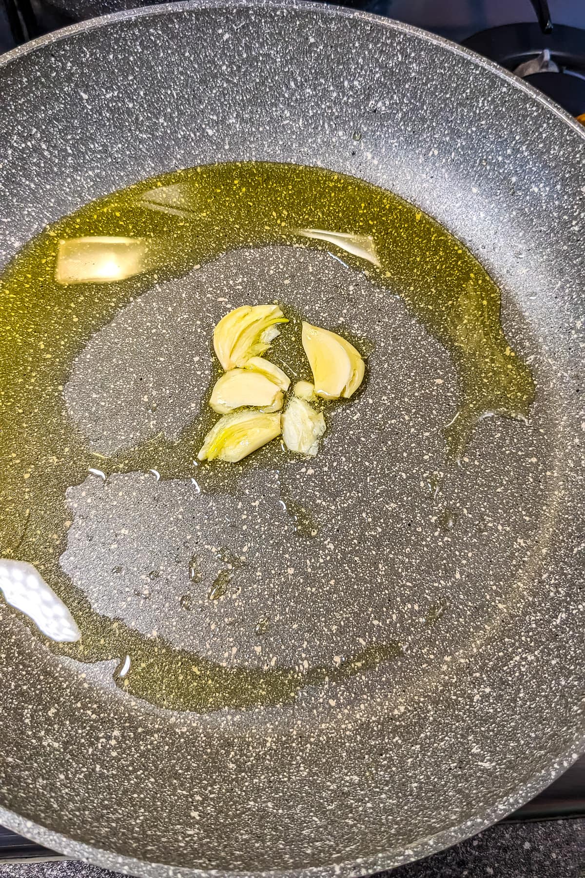 Frying garlic in olive oil on a frying pan on the stove.