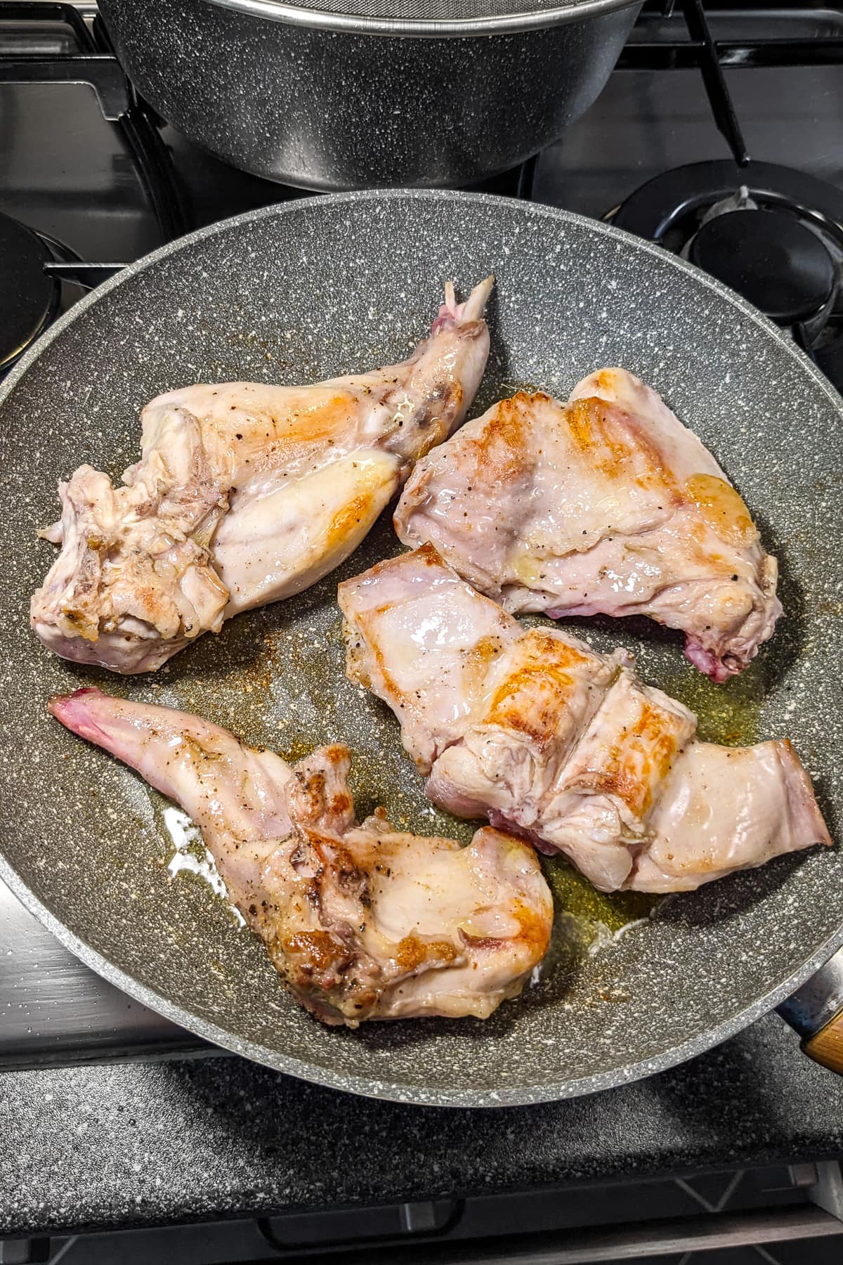 Fried rabbit meat on a stove in a frying pan.