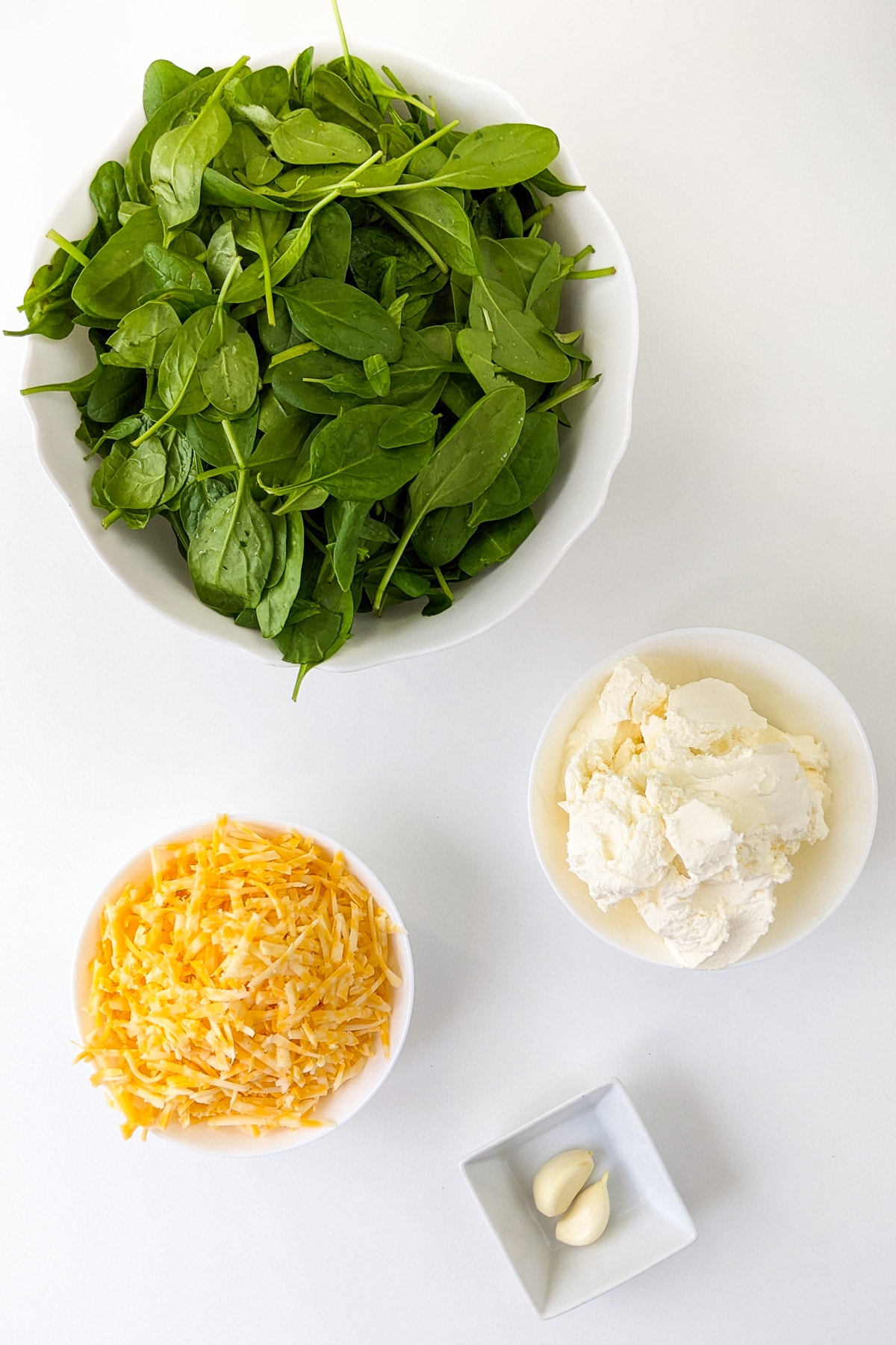 Large plate with fresh spinach near a plate with cheddar and cream cheese.