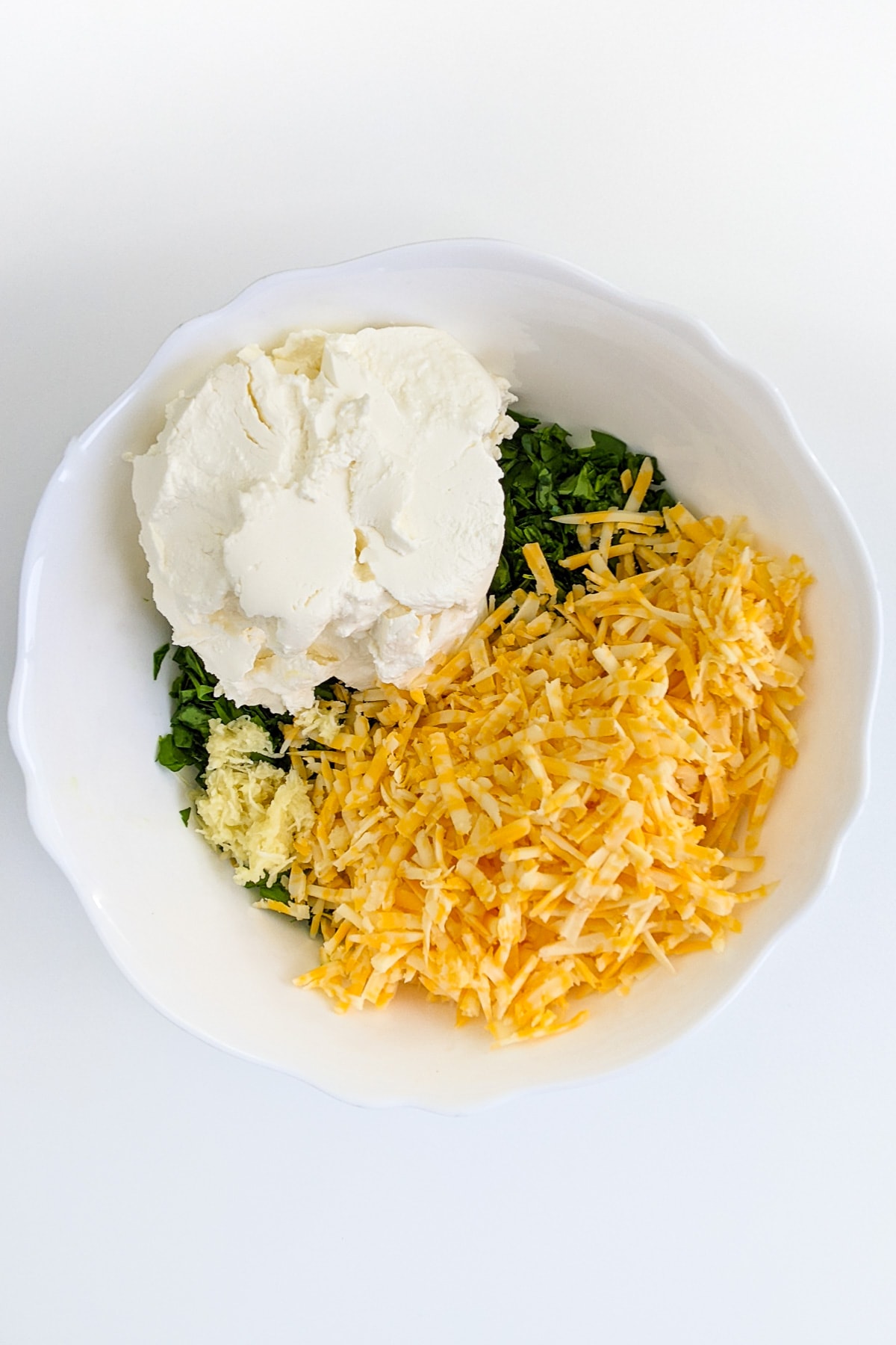 Top view of a white bowl with chopped parsley, cream cheese and cheddar.