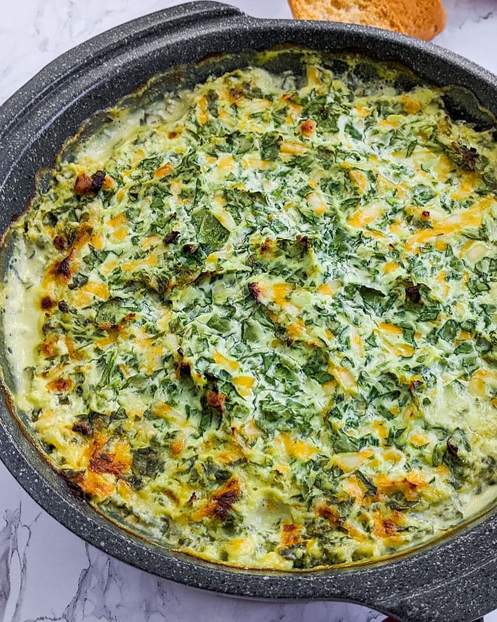 Close look of spinach dip in a gray baking dish.