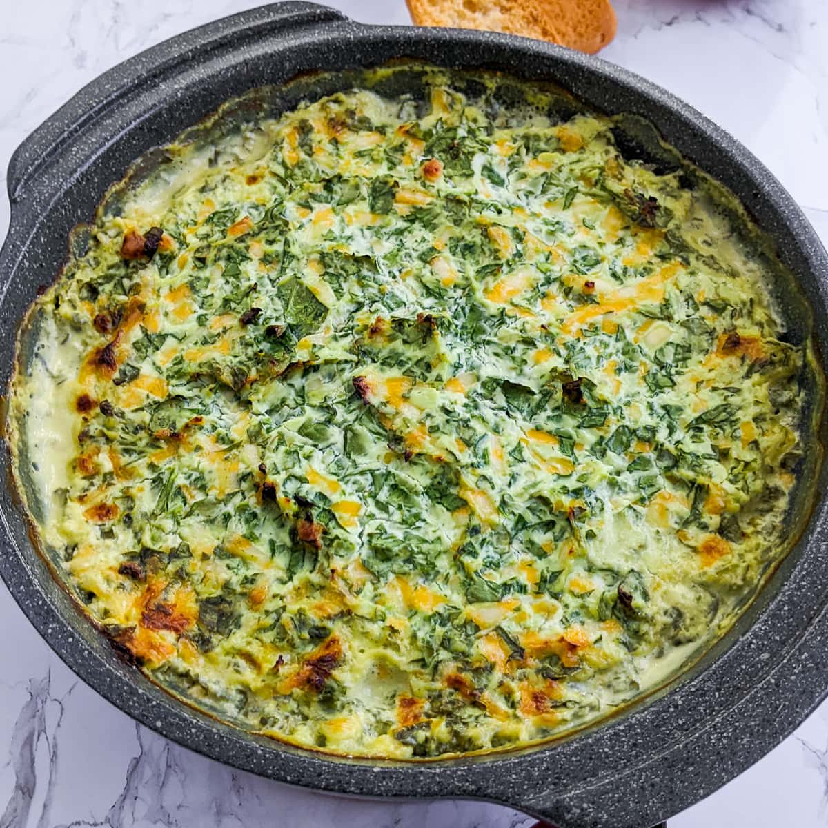 Close look of spinach dip in a gray baking dish.