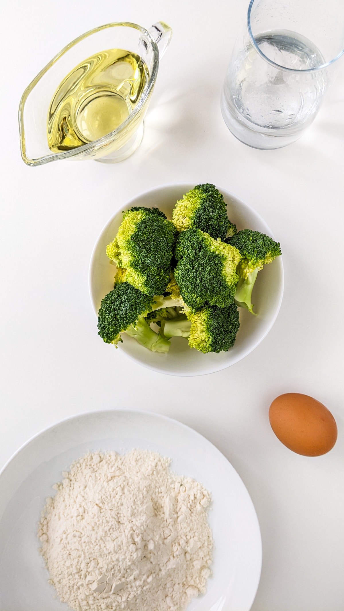 Top view of broccoli, oil, flour and an egg.