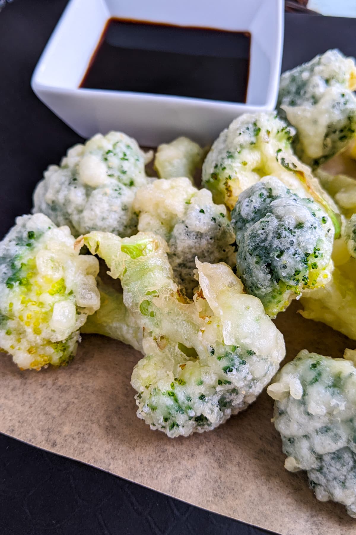 Close look of tempura broccoli near soy sauce.