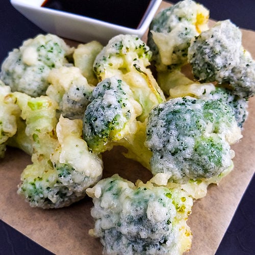 Close look of tempura broccoli near soy sauce.