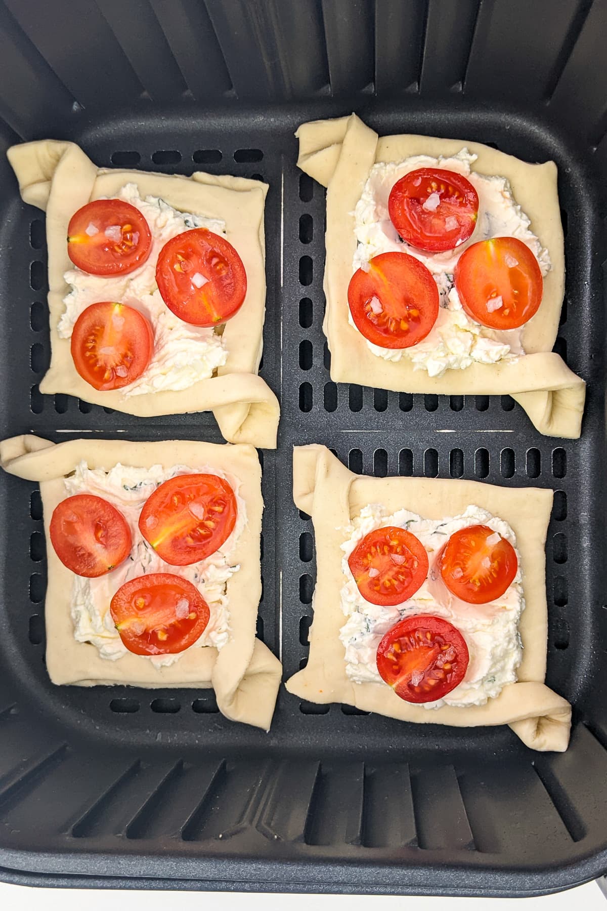 Top view of air fryer basket 4 tomato tartlets.