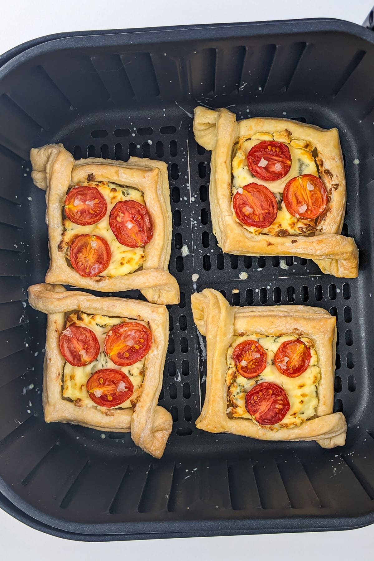 Top view of air fryer basket with 4 baked tomato tartlets.