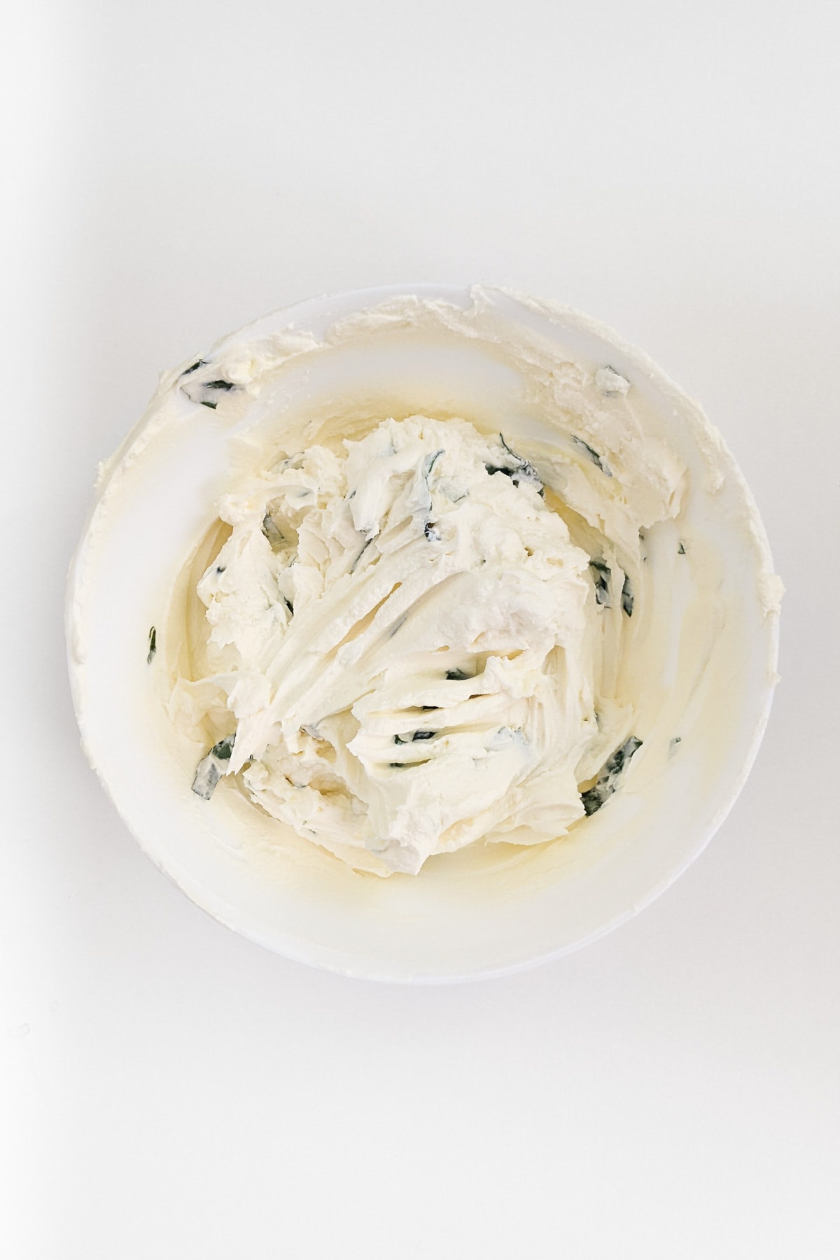 White plate with cream cheese and basil leaves.