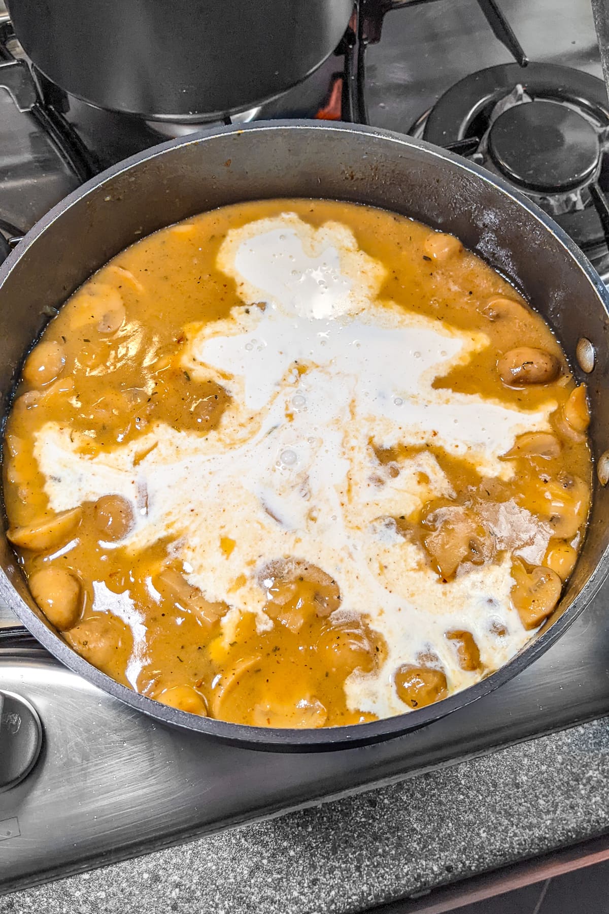 Adding cream over mushrooms sauce in a deep pan.
