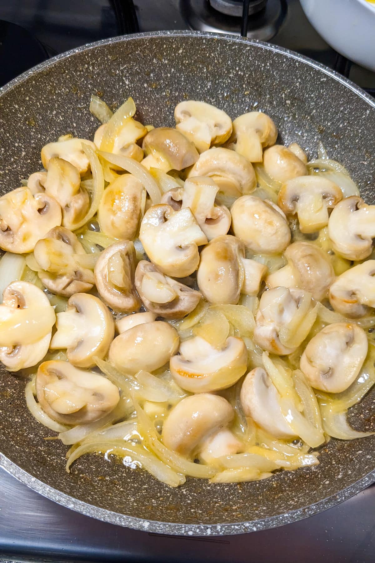 Fried onions and sliced mushrooms in a frying pan.