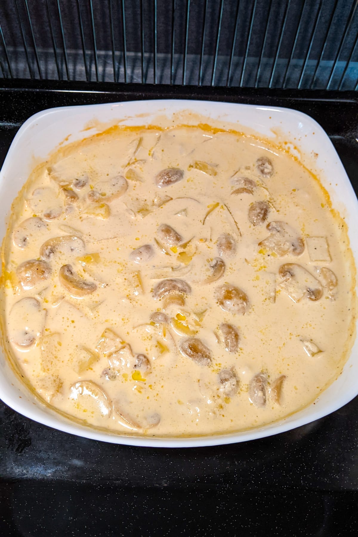 A plate with white sauce and different vegetables sitting in the oven.