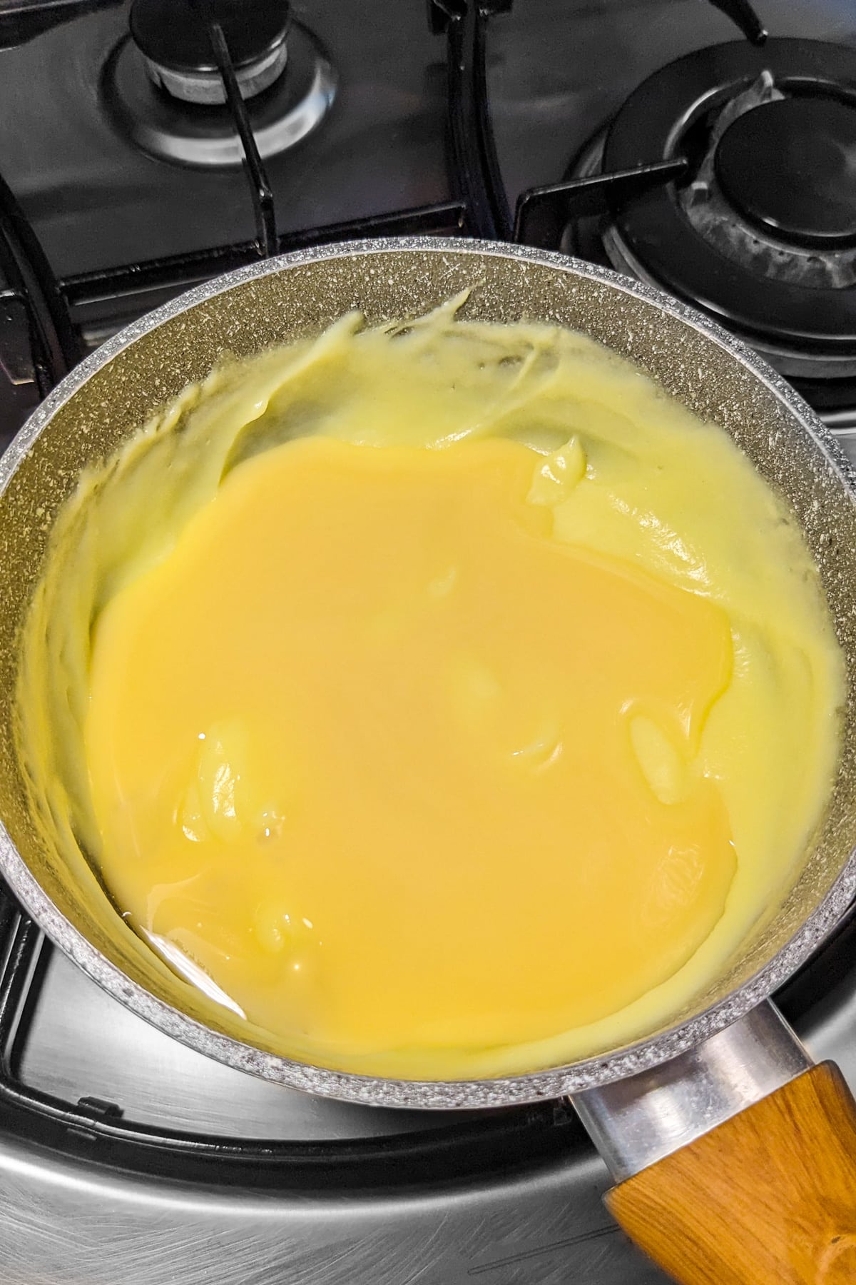 Condensed milk over creamy waffle sauce on a stove.