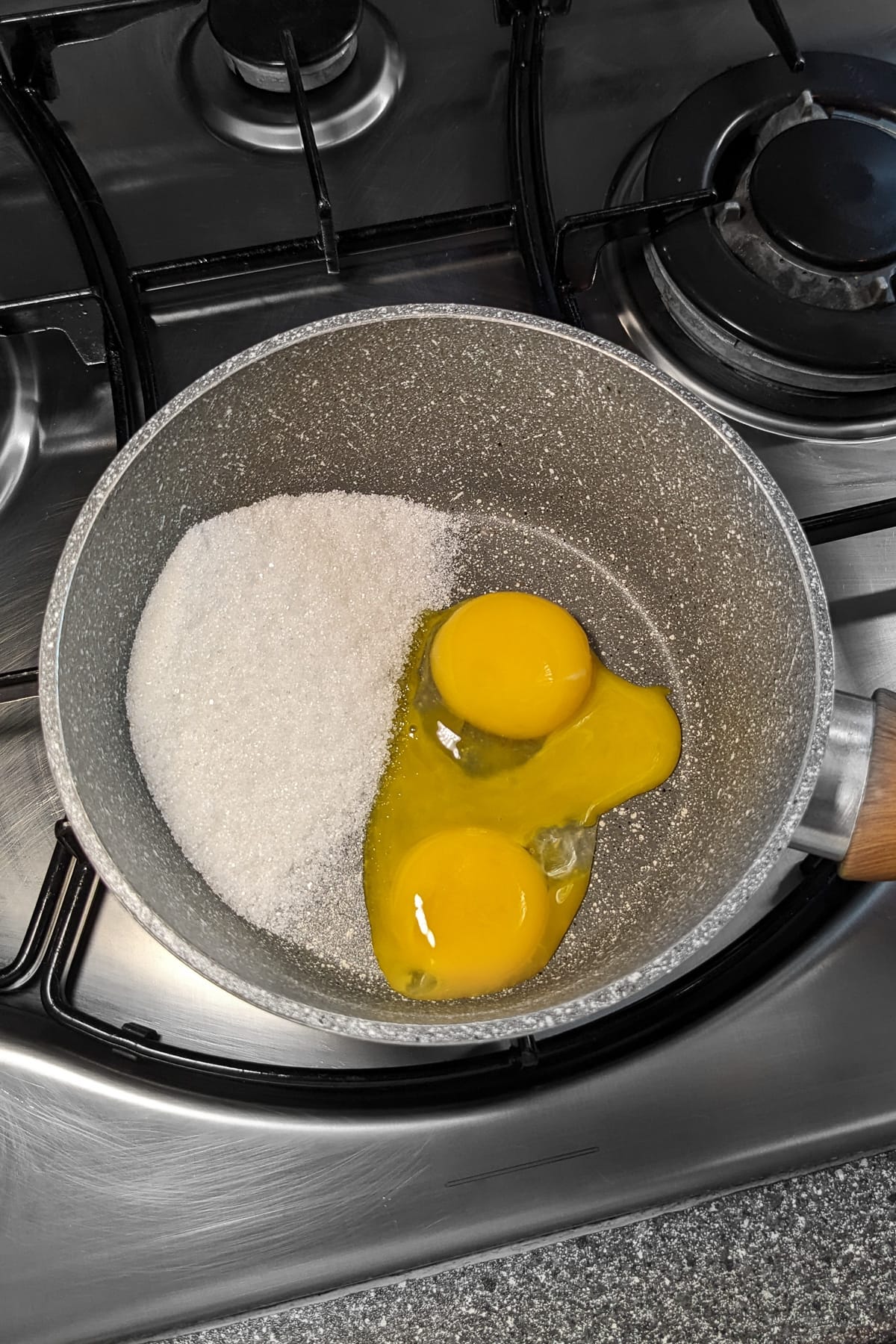 Sugar with two raw eggs on a stove in a sauce pan.