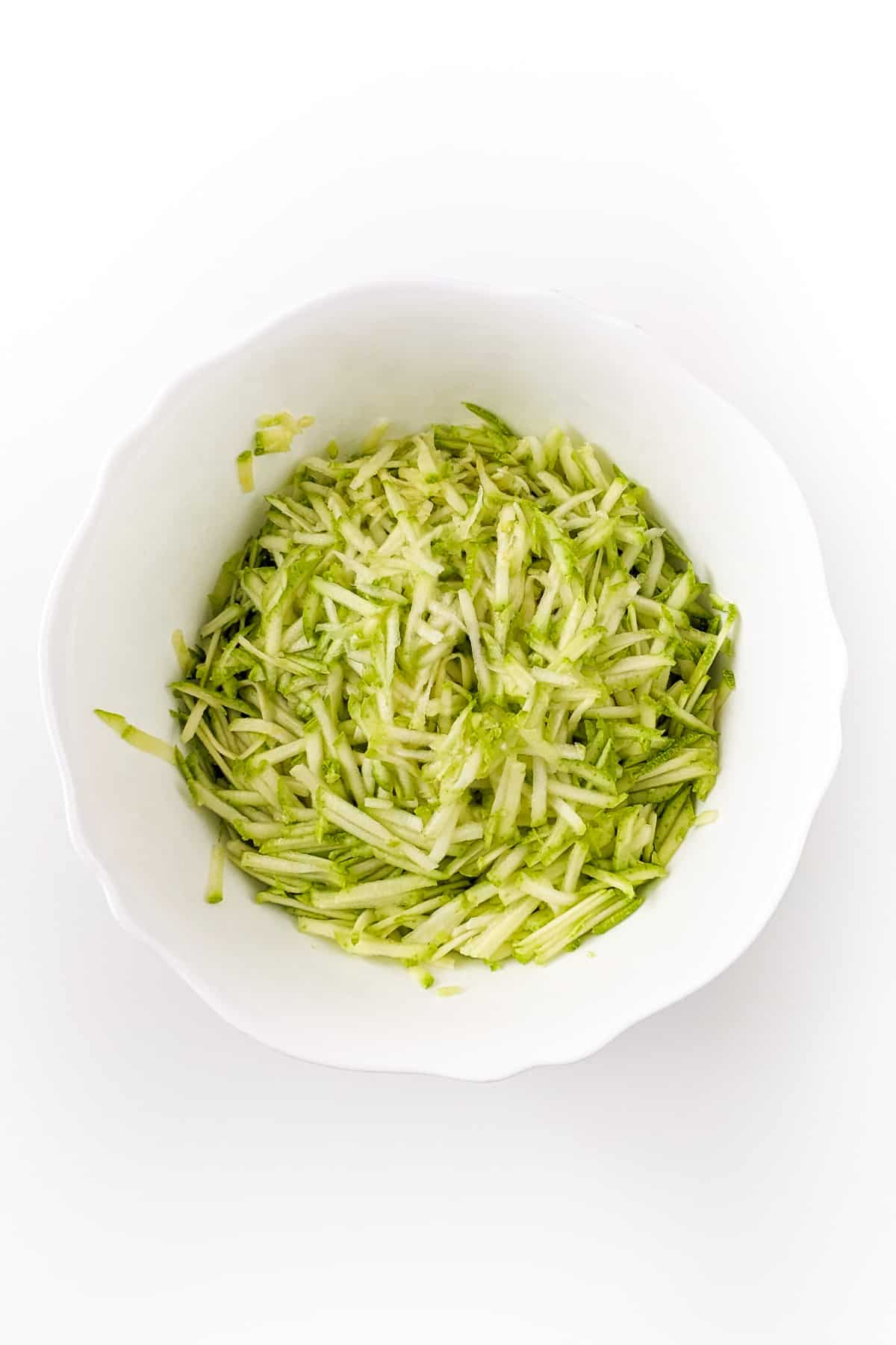 White deep bowl with shredded zucchini on a white background.