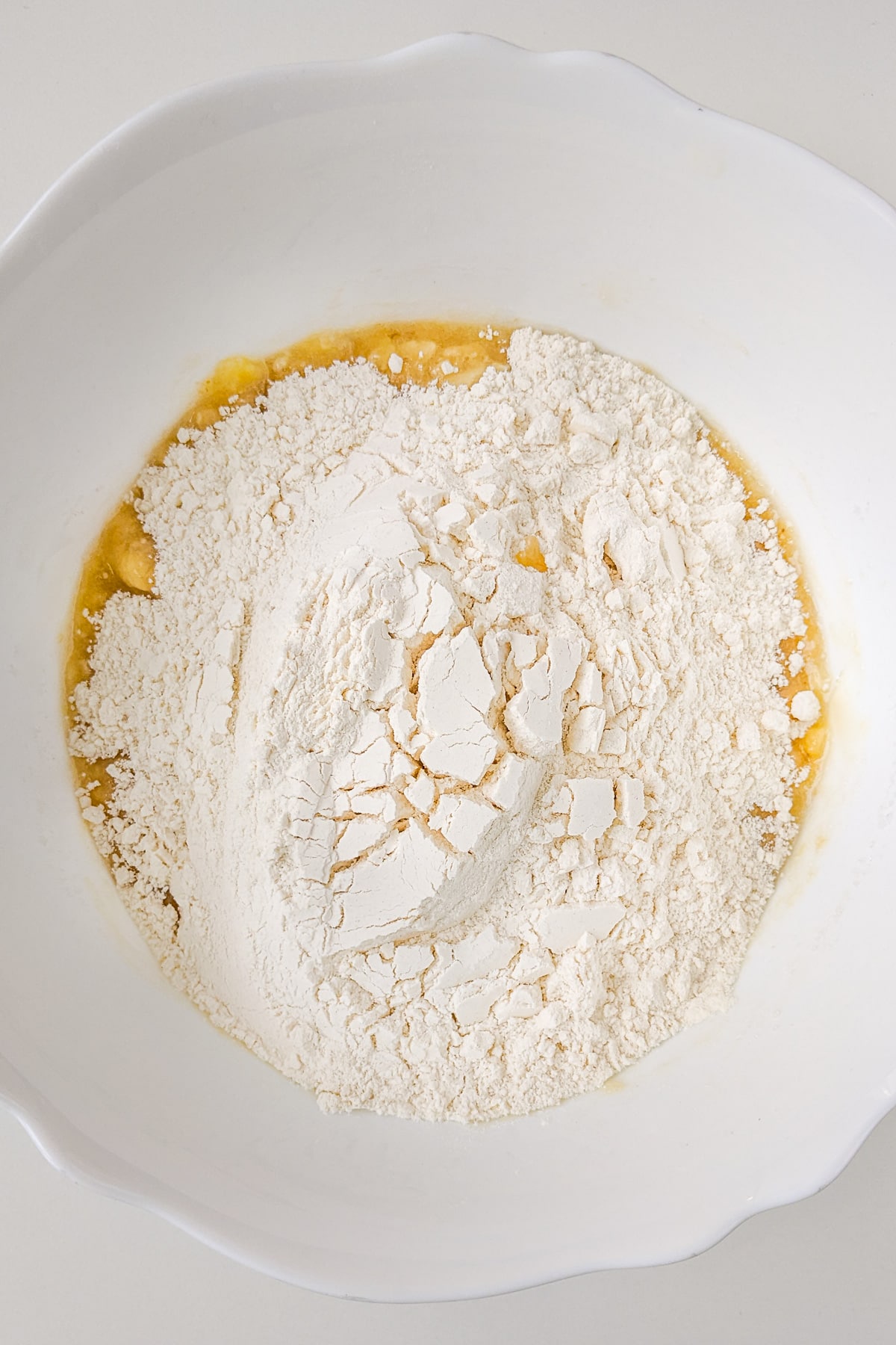 Flour over a mix of bananas and cane sugar in a white plate.
