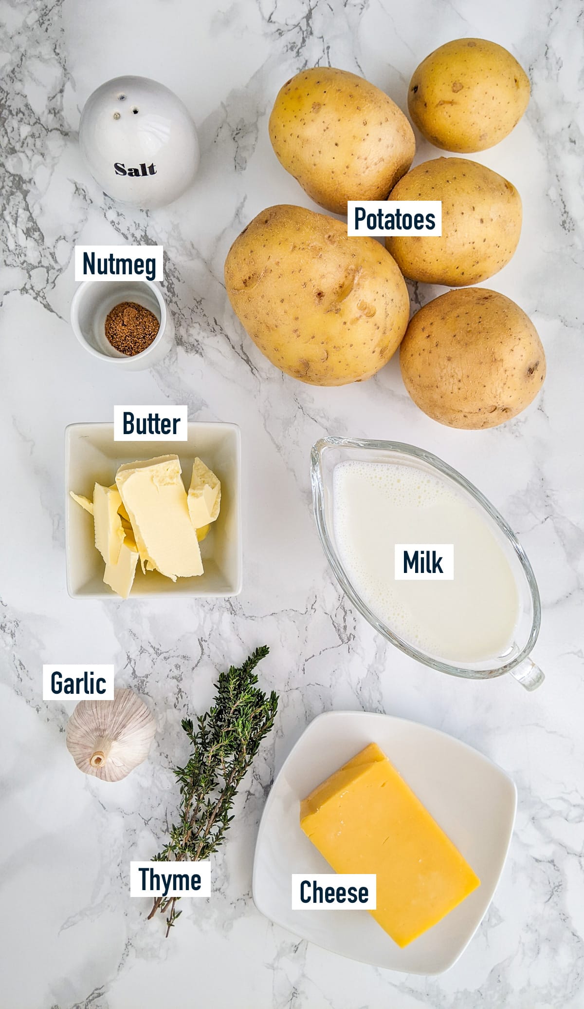 Potatoes, milk, cheese, butter, thyme and garlic on a marble table.
