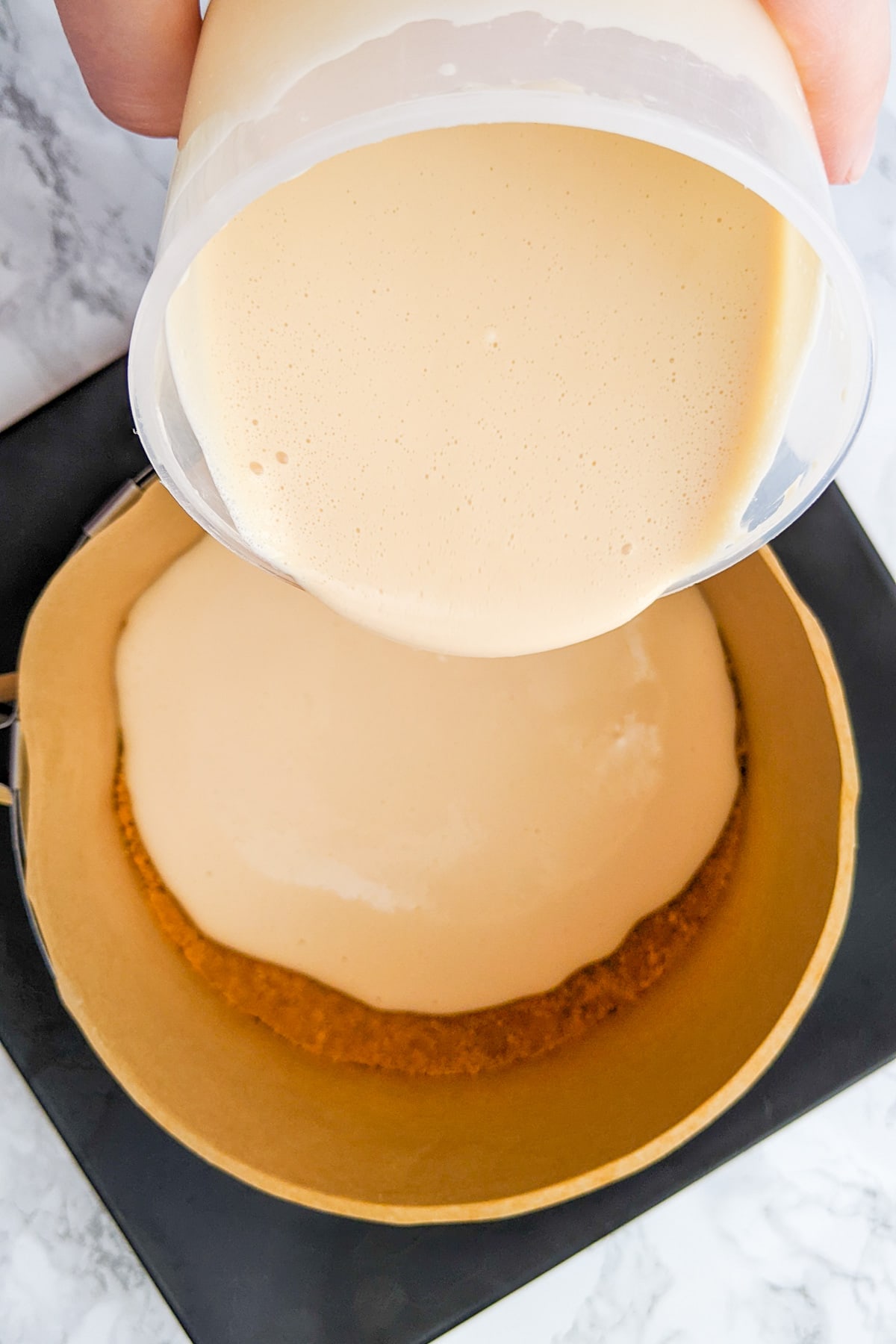 Pouring cream over a biscuit cheesecake layer.