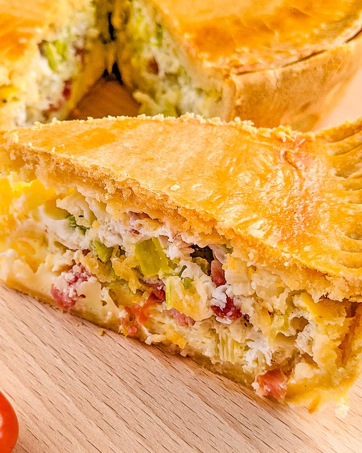 Close look of a slice of bacon and egg pie on a wooden board.