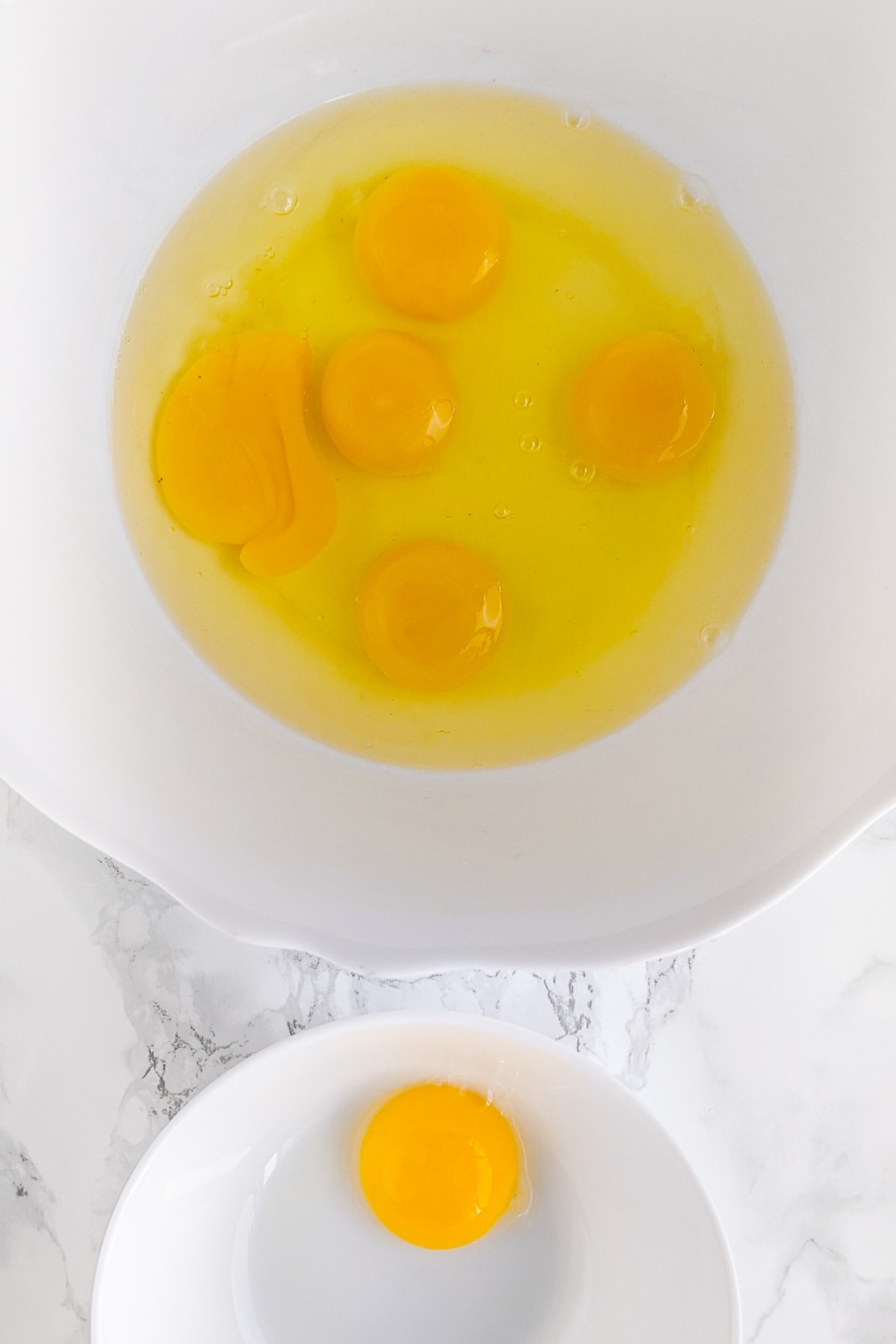 Two plates with raw eggs and one separate egg yolk.