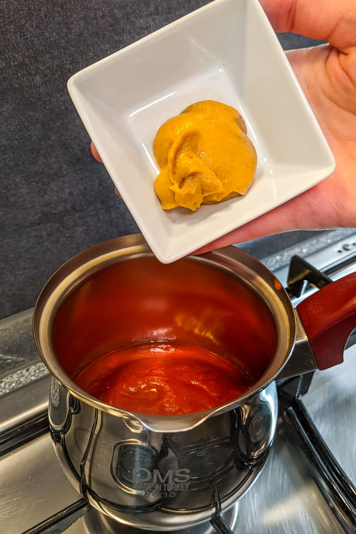 Pouring mustard in a sauce pan with ketchup.