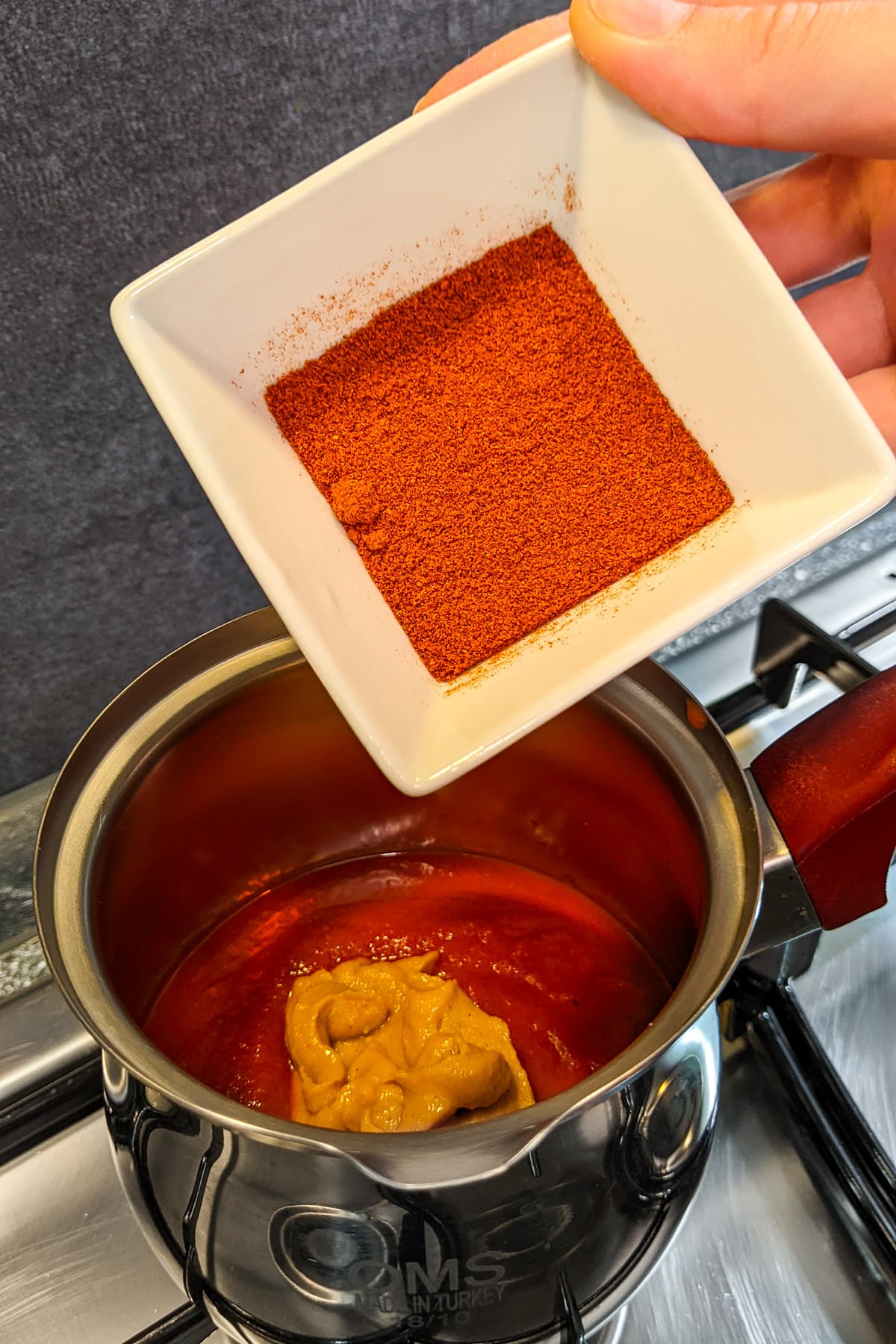 Woman hand holding a plate with smoked paprika over a sauce pan.