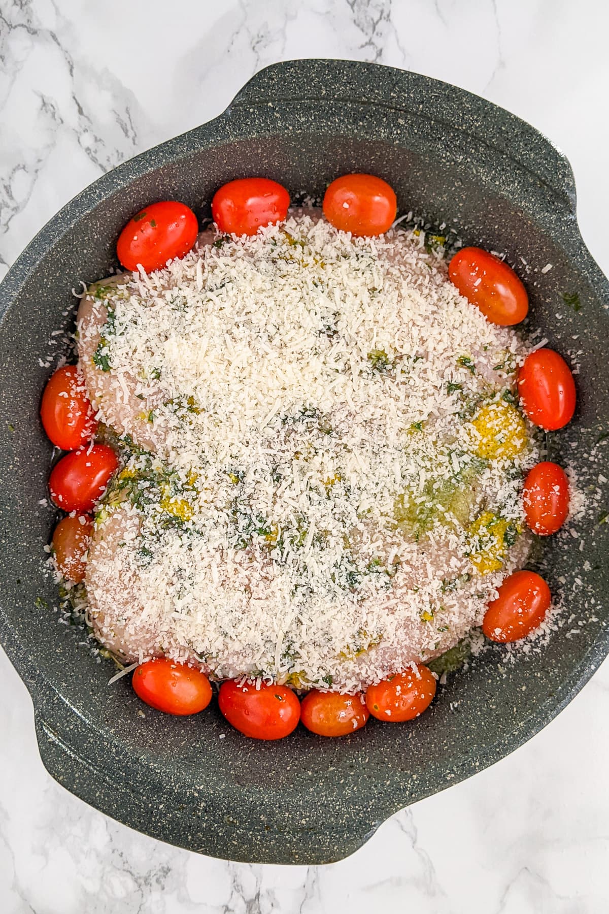 Top view of chicken breast in a casserole with tomatoes and topped with parmesan.
