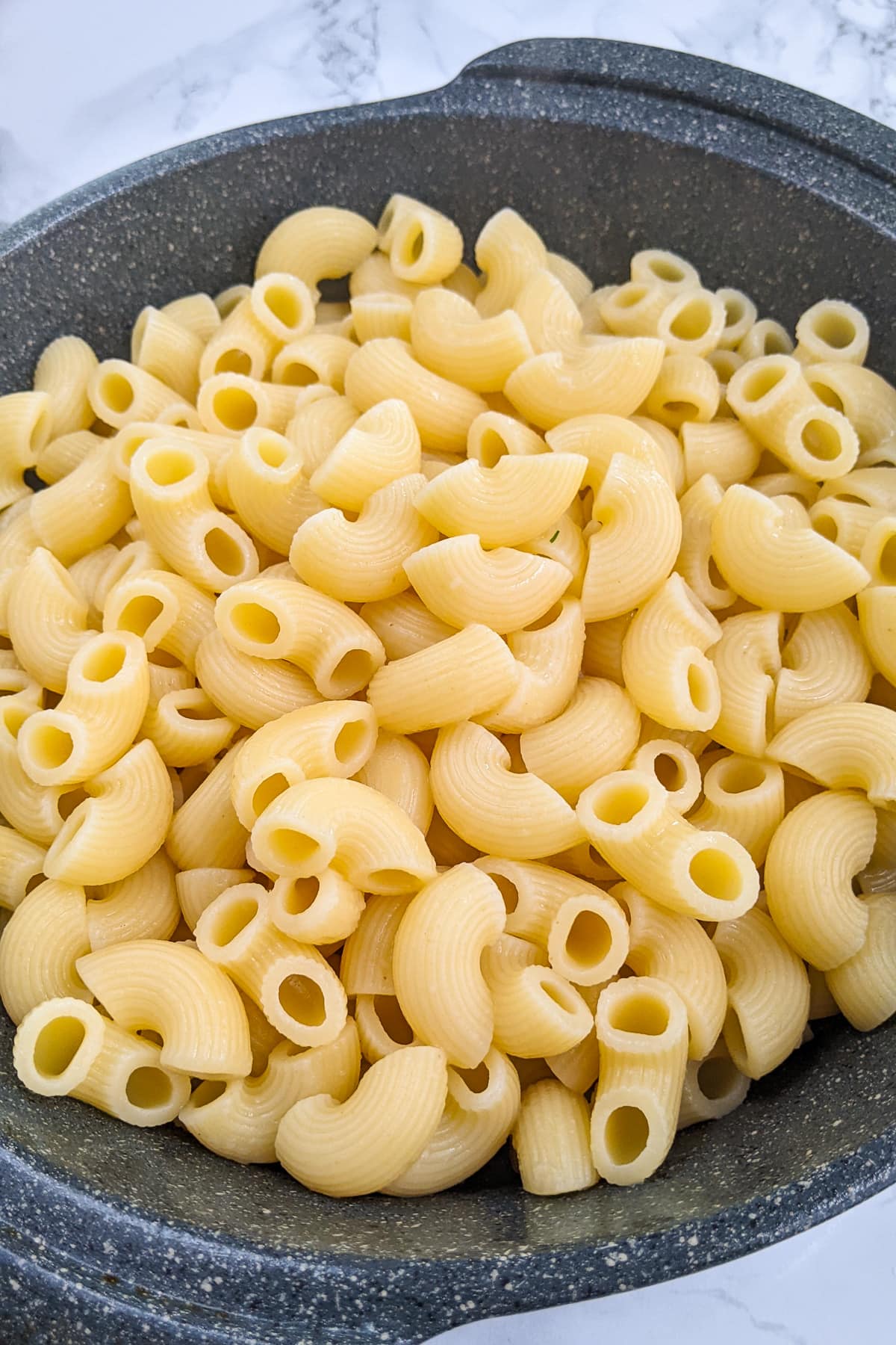 Close look of boiled macaroni pasta in a gray casserole.
