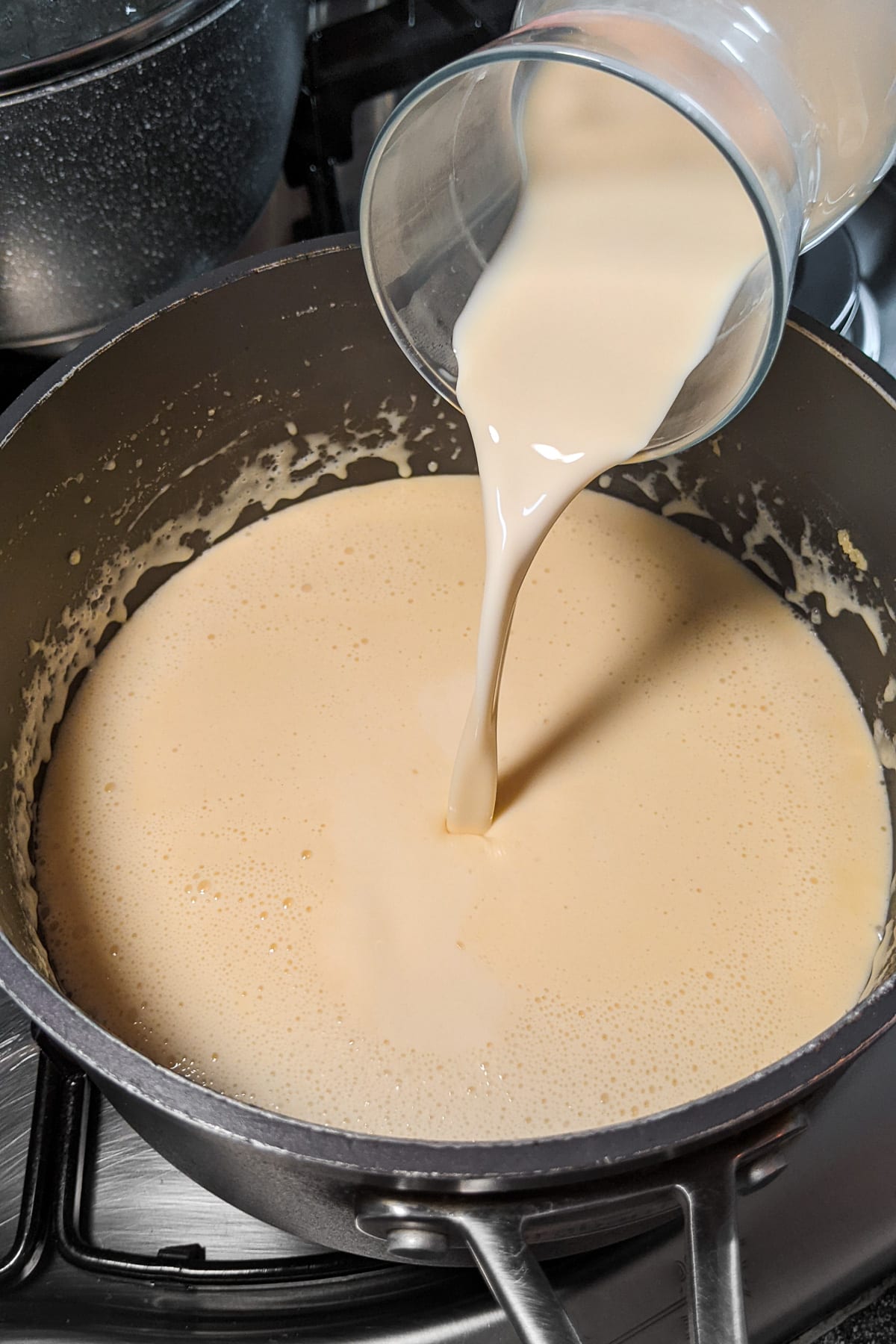 Pouring evaporated milk in a mac and cheese sauce.