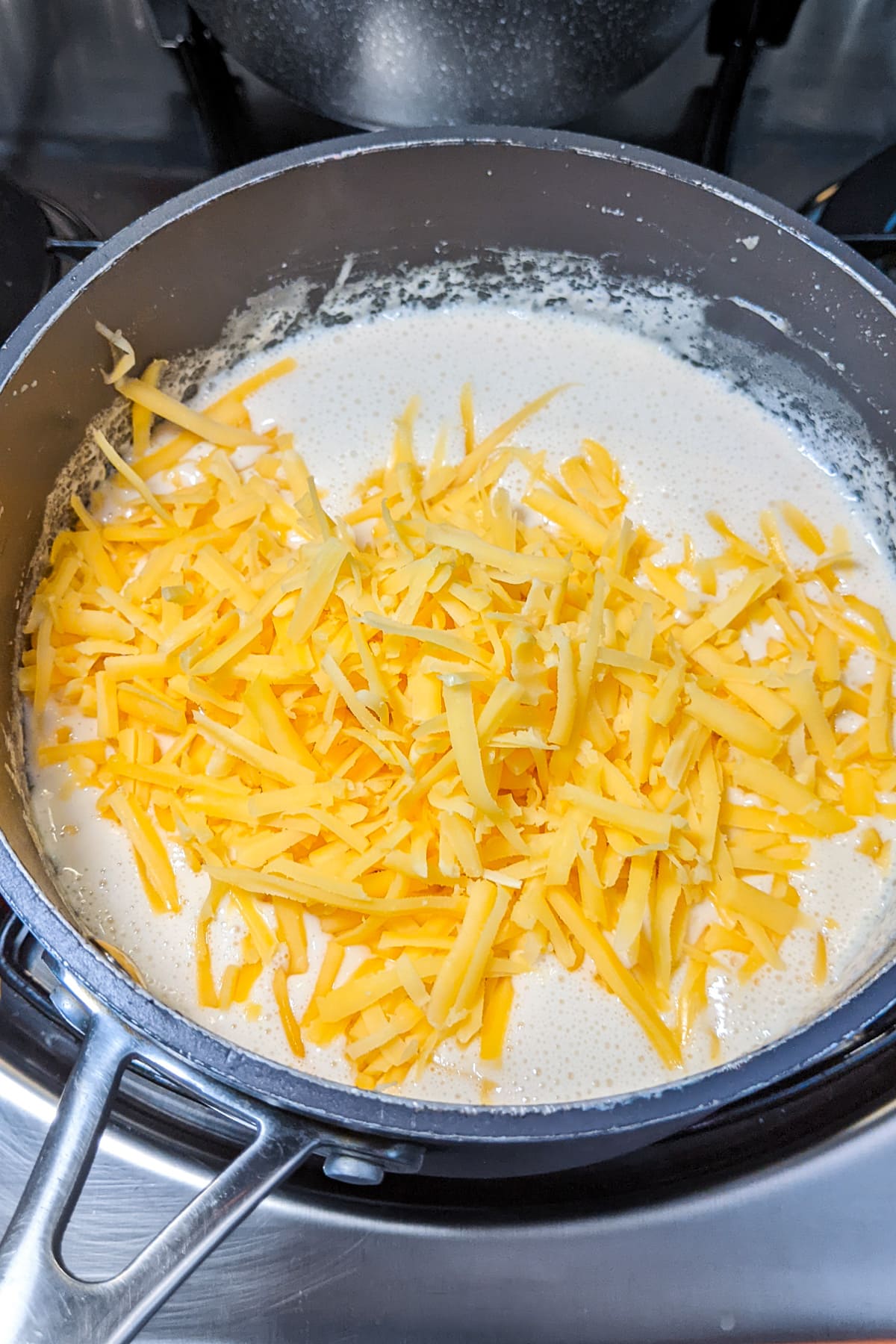 Shredded cheddar cheese over creamy sauce in a pan on the stove.