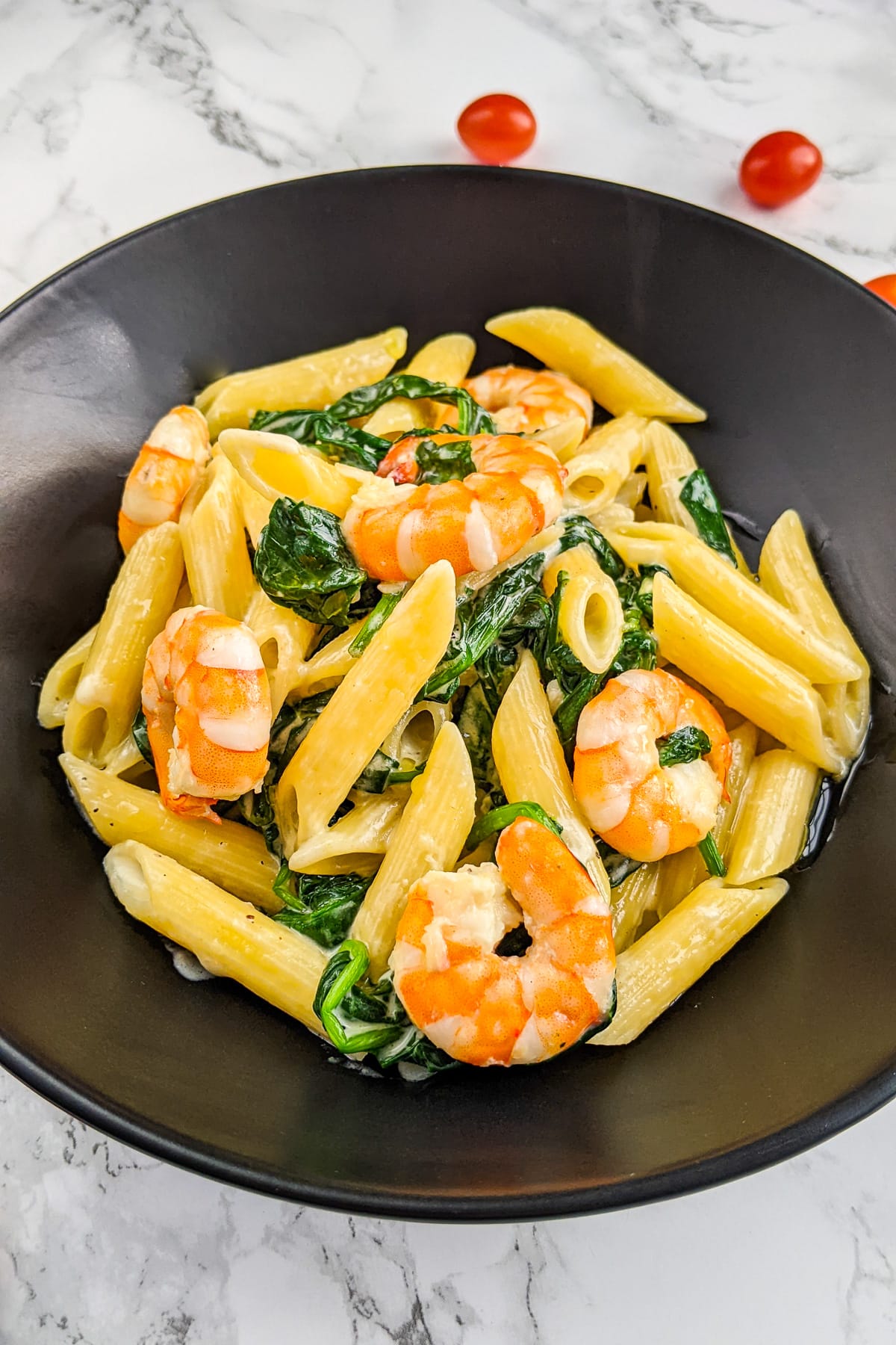 Close look of a black plate with creamy pasta, prawns and spinach.